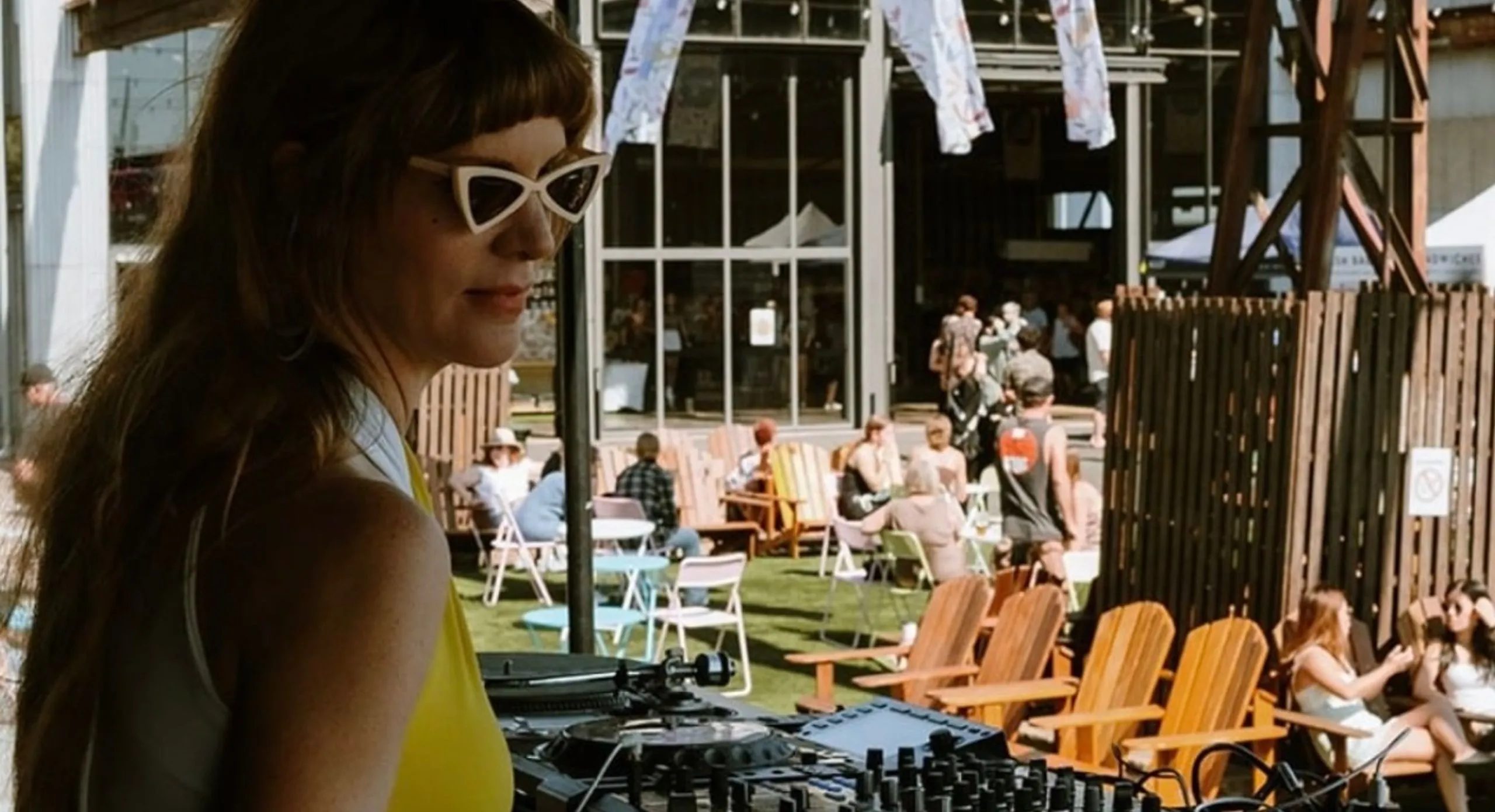 DJ playing on Pioneer CDJs at an outdoor event, with deck chairs and a crowd behind