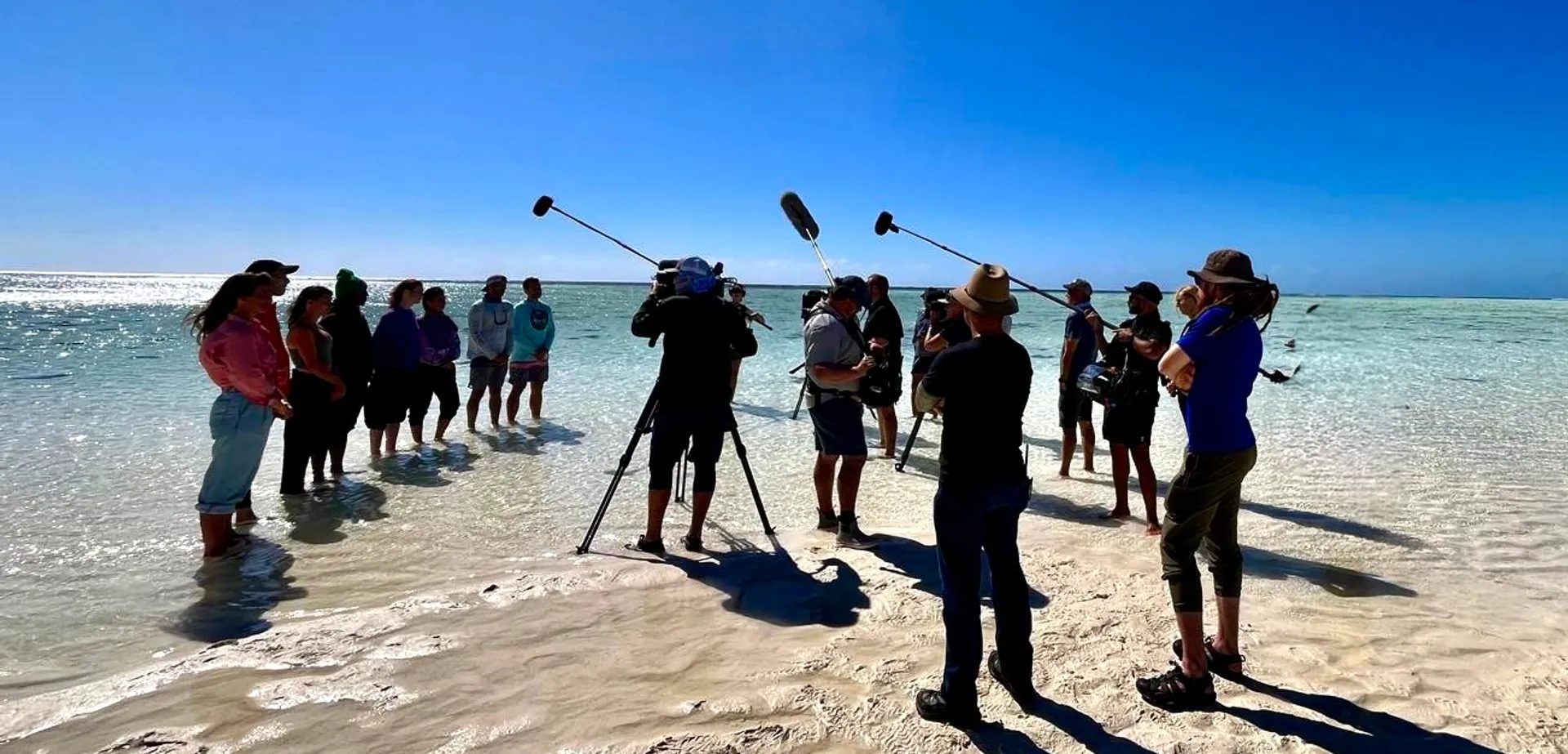 Location sound crew with three boom mics up on a white sandbank while filming All the Sharks