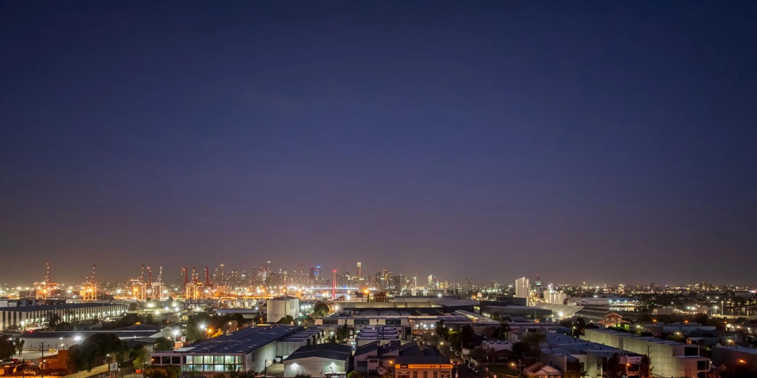 Drone view over Footscray at dusk, looking across to the Melbourne CBD skyline and the port cranes
