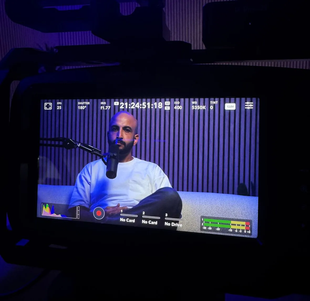 Mike Jaballah on camera in the podcast studio, shown on a Blackmagic monitor with a blue LED accent