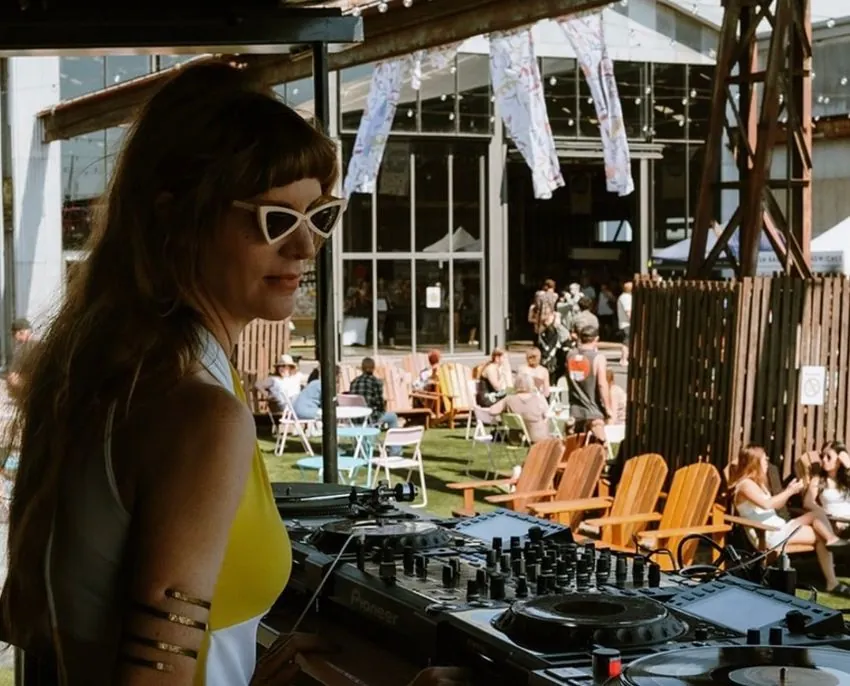 DJ playing on Pioneer CDJs at an outdoor event, with deck chairs and a crowd behind