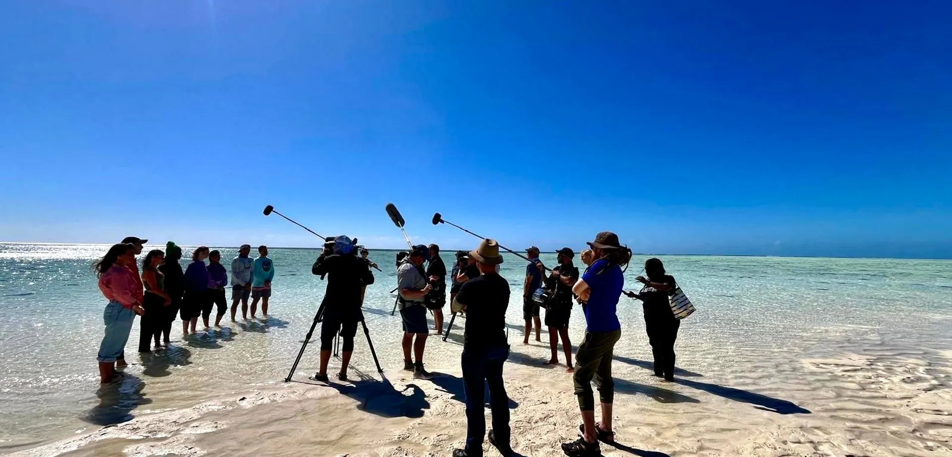 Location sound crew with three boom mics up on a white sandbank while filming All the Sharks