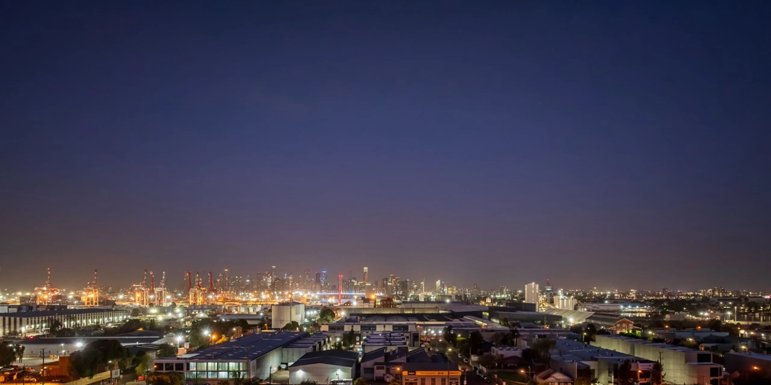 Drone view over Footscray at dusk, looking across to the Melbourne CBD skyline and the port cranes