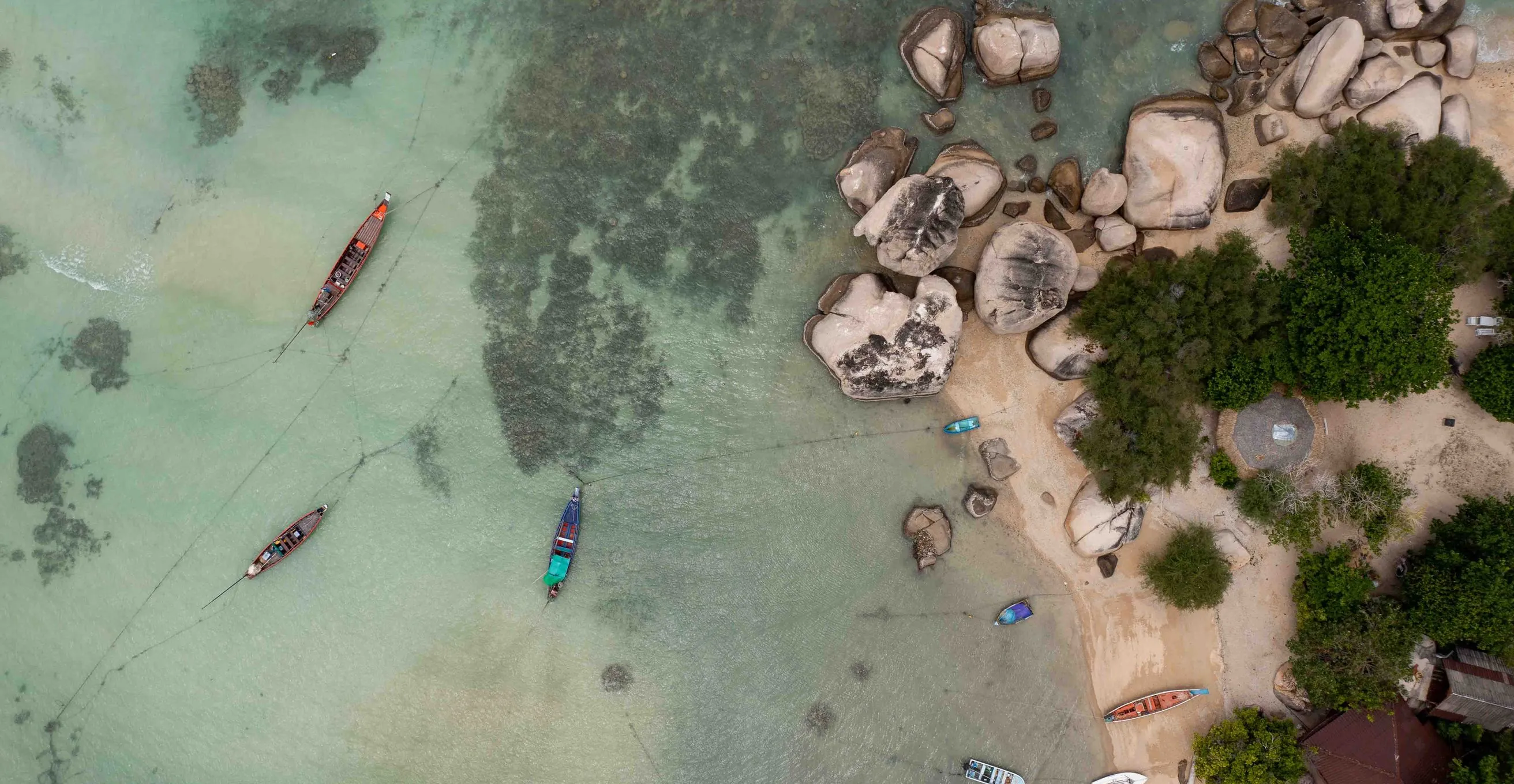 Top down drone view of boats beside a sand spit with huge boulders and clear aqua water at Koh Tao, Thailand