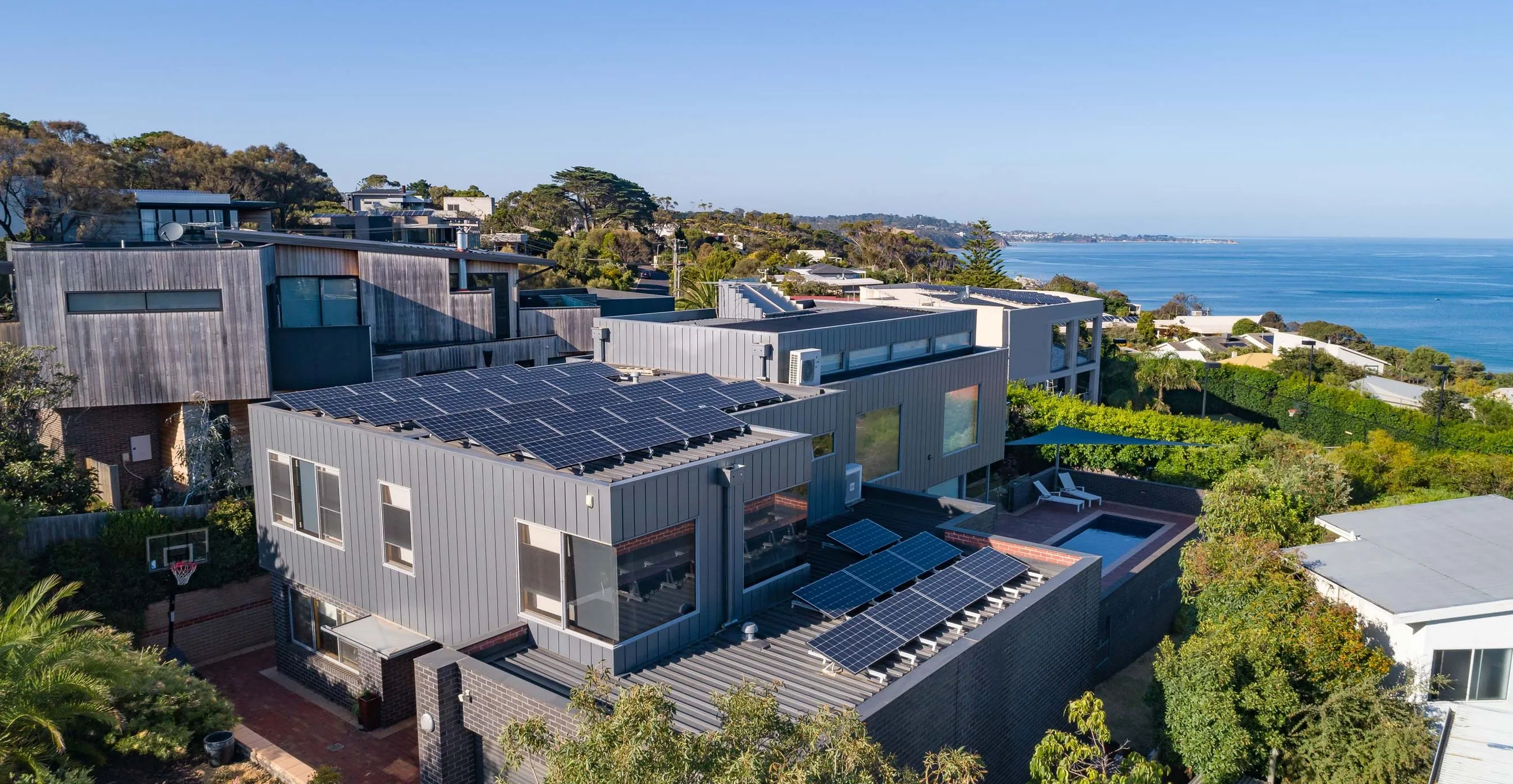 Drone view of a solar installation and a double storey house in Mornington, with Port Phillip Bay behind