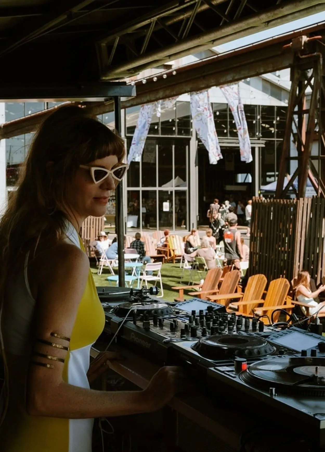DJ playing on Pioneer CDJs at an outdoor event, with deck chairs and a crowd behind