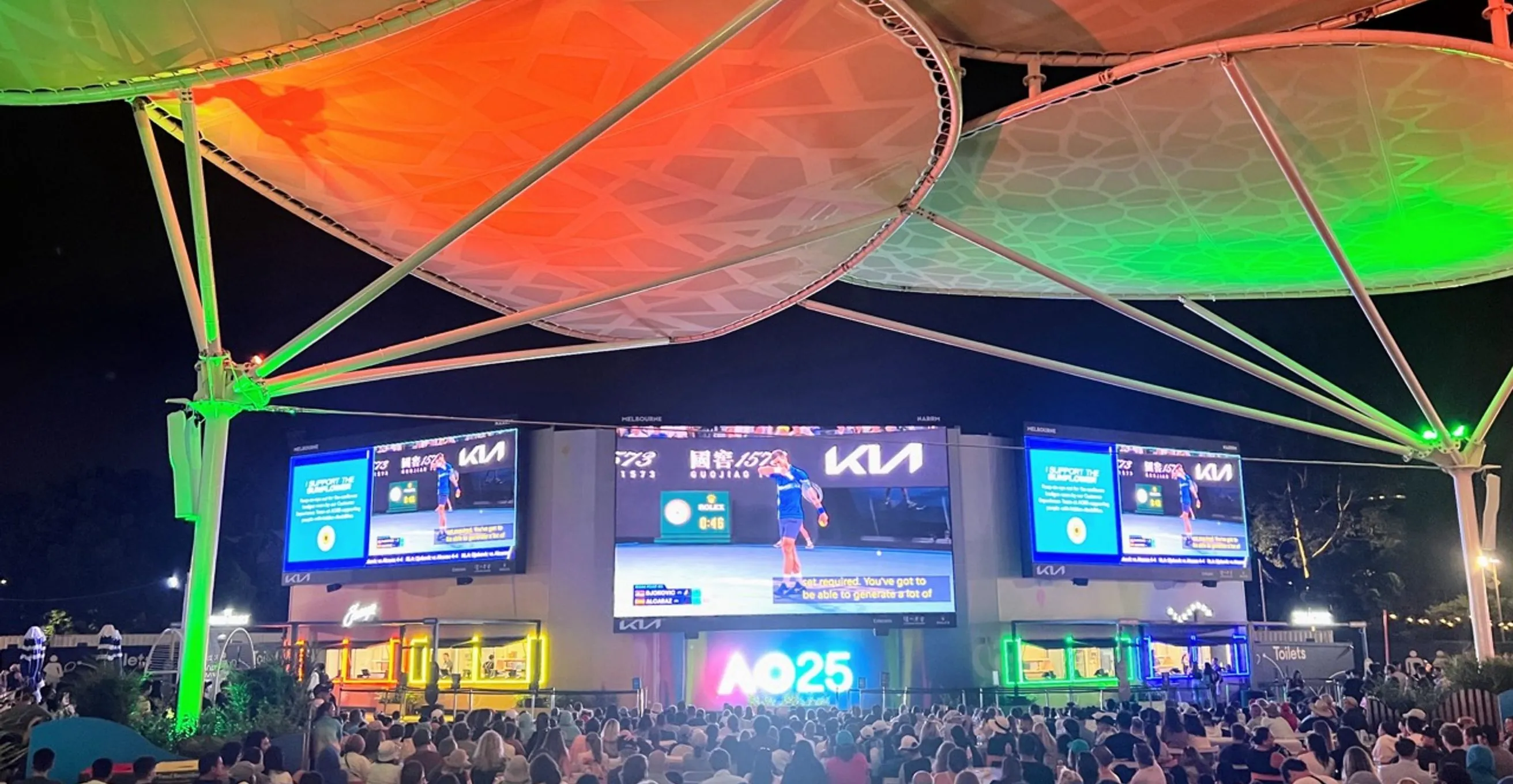 Crowd at the Australian Open fan zone at night, with big screens