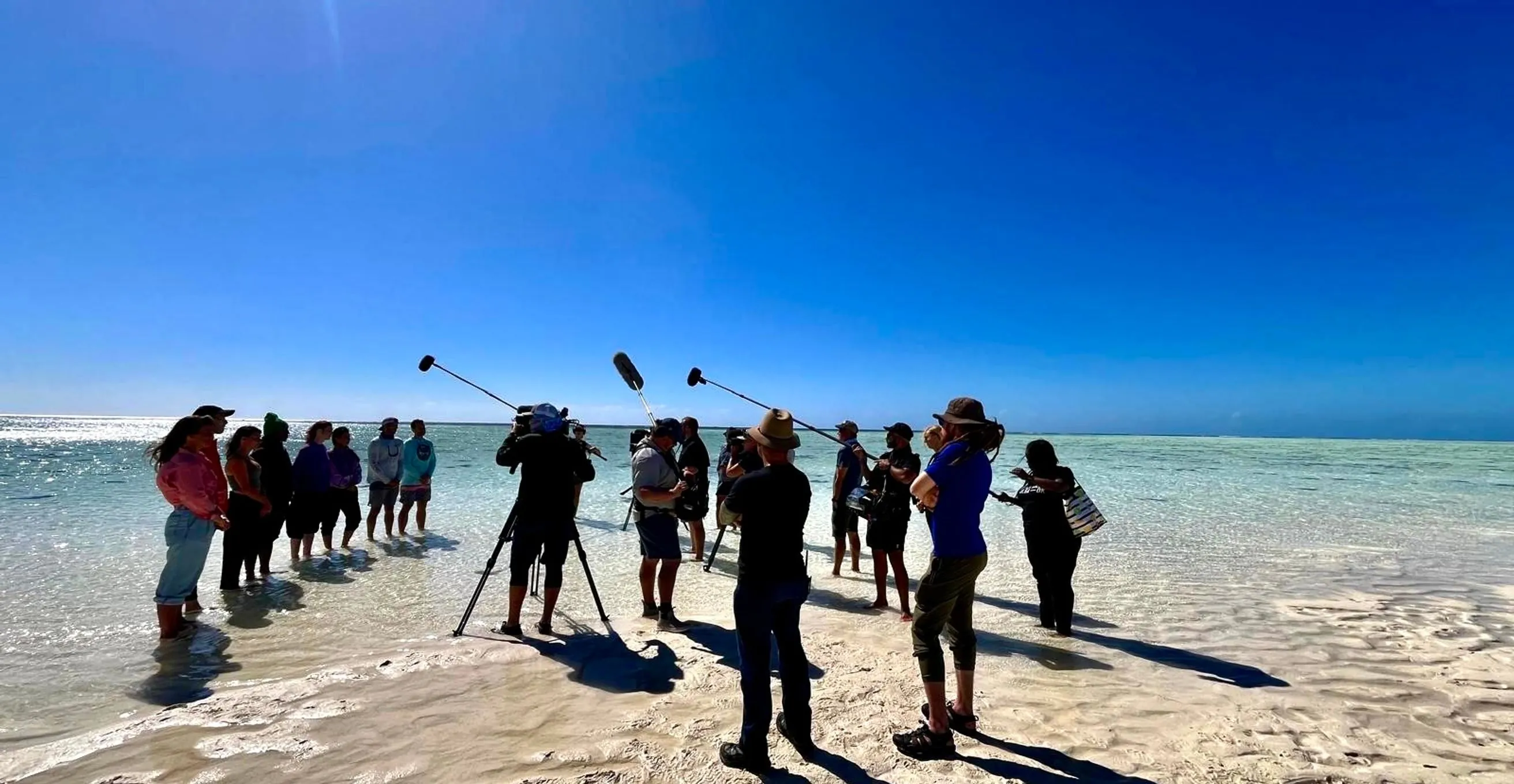 Location sound crew with three boom mics up on a white sandbank while filming All the Sharks